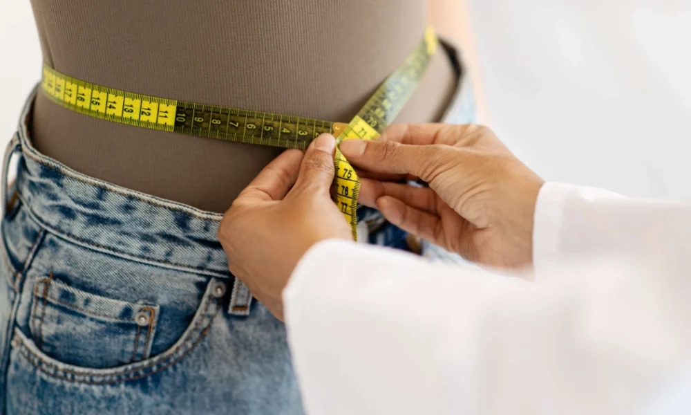 A healthcare professional measures a person's waist with a yellow tape during a Medically Managed Weight Loss Program in O'Neill, NE.