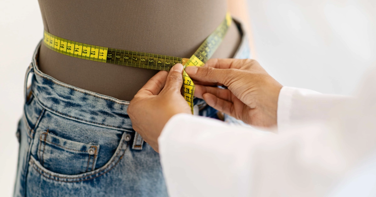 A healthcare professional measures a person's waist with a yellow tape during a Medically Managed Weight Loss Program in O'Neill, NE.